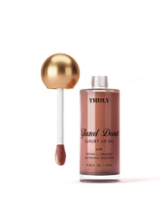 A bottle of Truly Beauty Luxury Peptide Lip Oils with a gold-capped applicator wand sits against a pale white background. The bottle holds 0.42 fl. oz. (12 ml) of product.