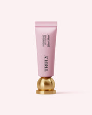 A pink tube of Truly Beauty Hydrating Lip Gloss with hyaluronic acid stands upright on a round, gold base against a light pink background.
