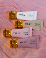 Collection of 'TRULY' lip glosses on a pink fabric background