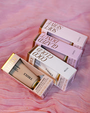 Makeup products including lipsticks and a foundation on a pink fabric background