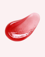 A glossy, teardrop-shaped droplet of The Luxury Peptide Lip Oils by Truly Beauty, in translucent red with tiny bubbles inside, rests on a plain light pink background.