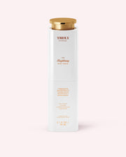 A white bottle of Truly Beauty’s The Brightening Body Serum, featuring a gold cap and minimalist design, stands upright against a pale pink background—specially formulated to target dark spots and hyperpigmentation.