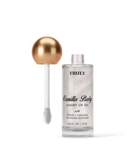 A bottle of Truly Beauty Luxury Peptide Lip Oil with a gold spherical cap and applicator wand sits against a pale white background. The clear bottle reveals the shimmery oil inside.