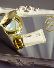 Gold lip gloss container with a tube of 'Truly' lip balm on an ornate surface.