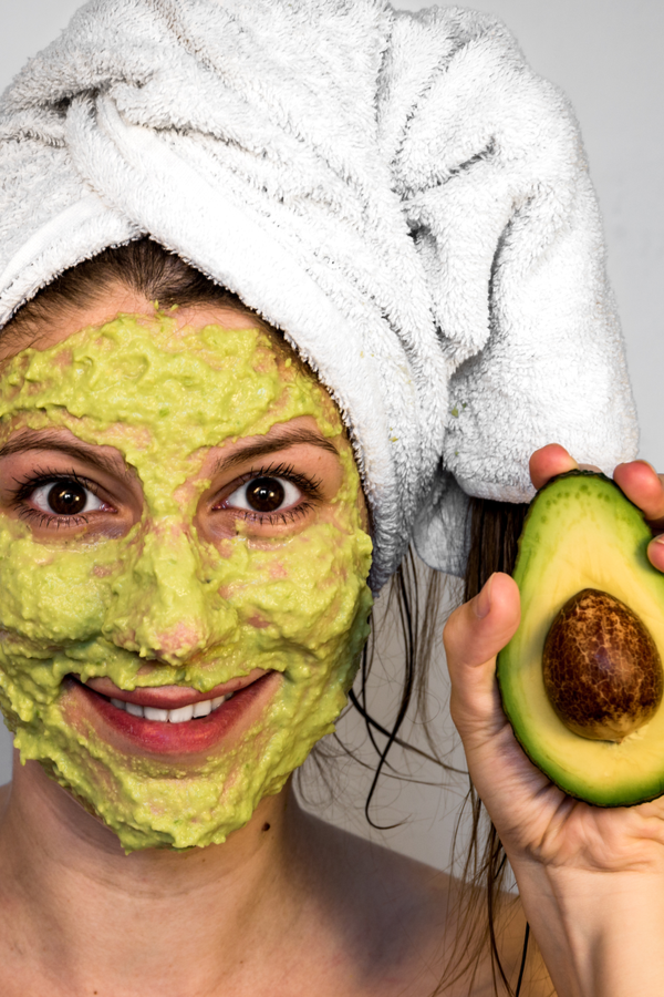 Woman with avocado face mask holding avocado