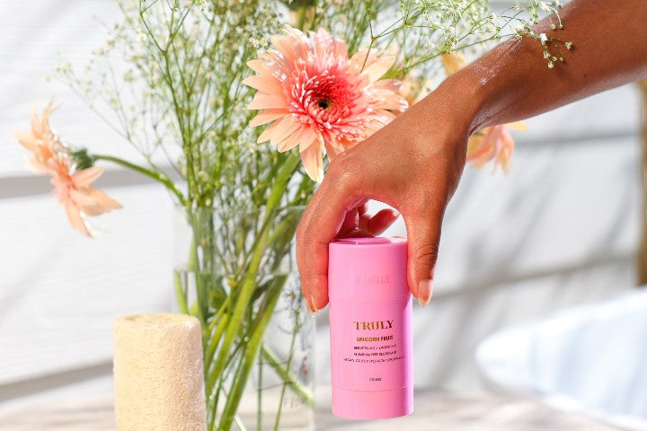 Truly Unicorn Fruit Skin Brightening Deodorant held up in front of flowers