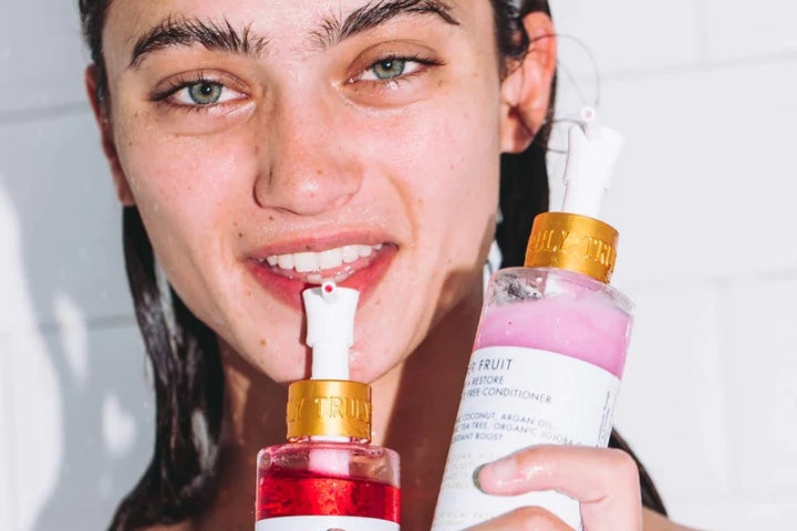 young woman with wet hair holding Truly's shampoo and conditioner