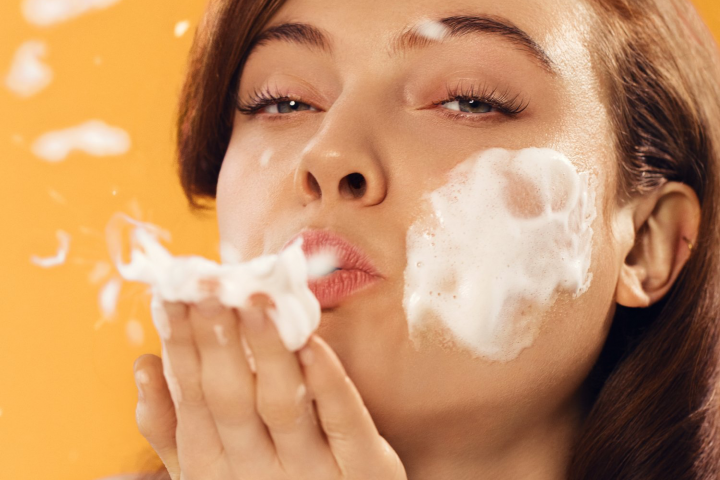 Young woman blowing foam cleanser on hand