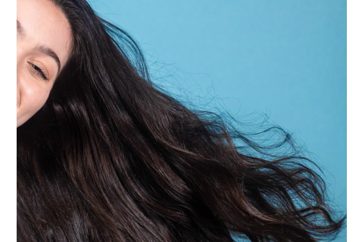 Closeup of young woman with dark brown hair with blue background | what does glycolic acid do for hair