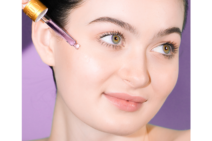 young woman's face with serum dropper pressed against cheek