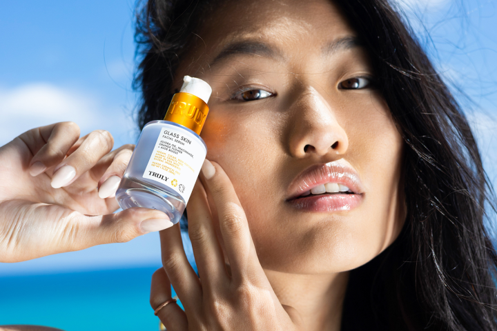young woman with dark hair holding Truly's glass skin facial serum