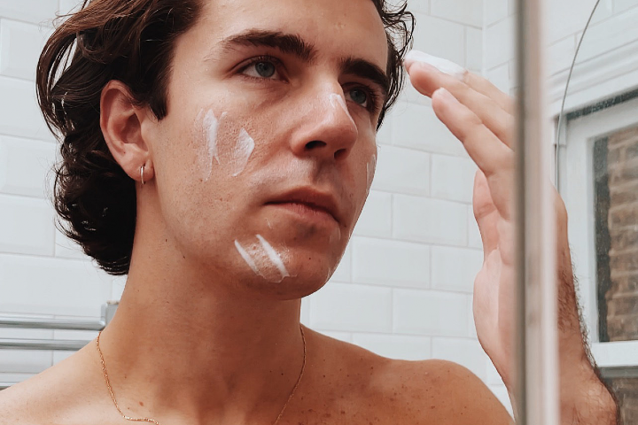 Young man with long hair applying cream to face