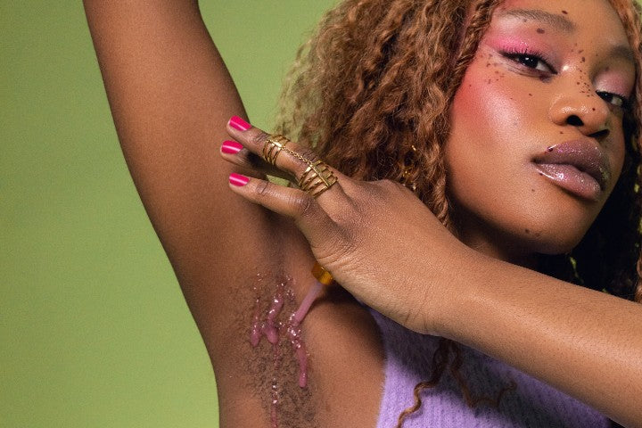 Young woman applying pink serum to underarm area with dropper