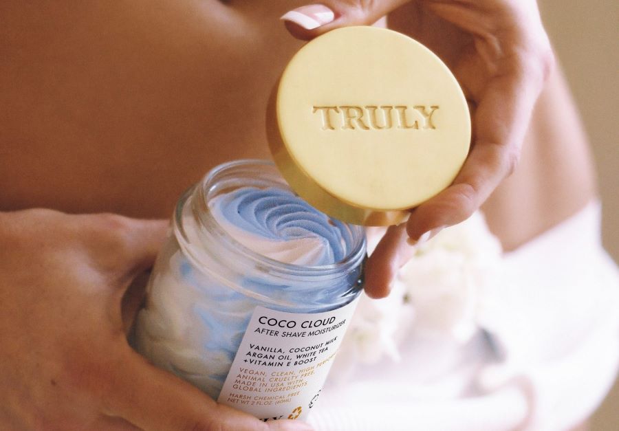 benefits of mango butter for skin | Woman holding open jar of Truly's coco cloud after shave moisturizer