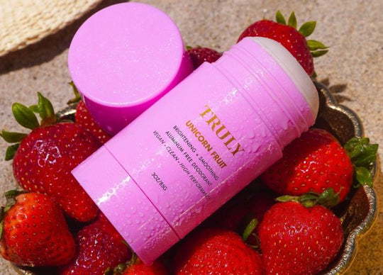 A hand holds a bottle from the Truly Beauty Body Brightening Set above a pink background, with two more serums, an open moisturizer jar, and serum drops for how to get even skin tone on body