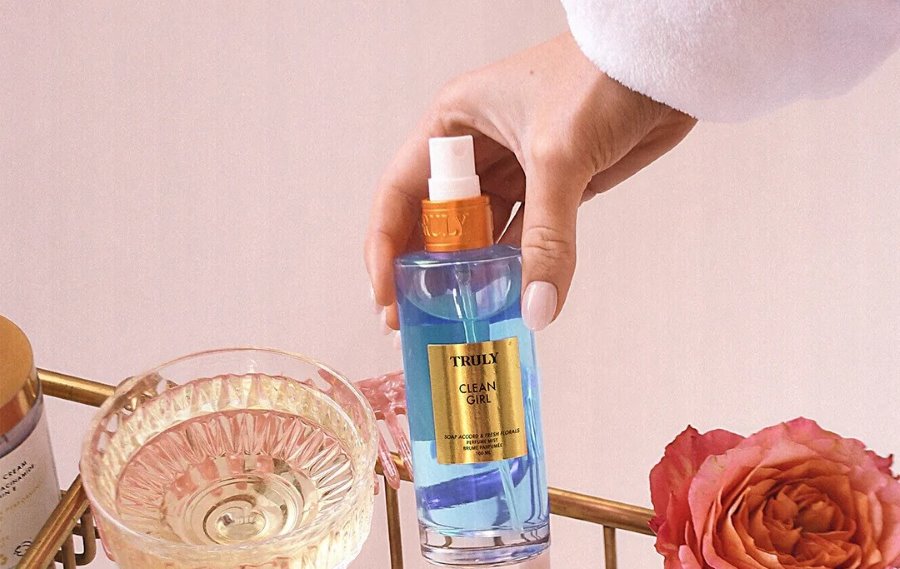 best clean perfume scents 2025 | woman's hand holding Truly's clean girl perfume mist with rose and glass in background