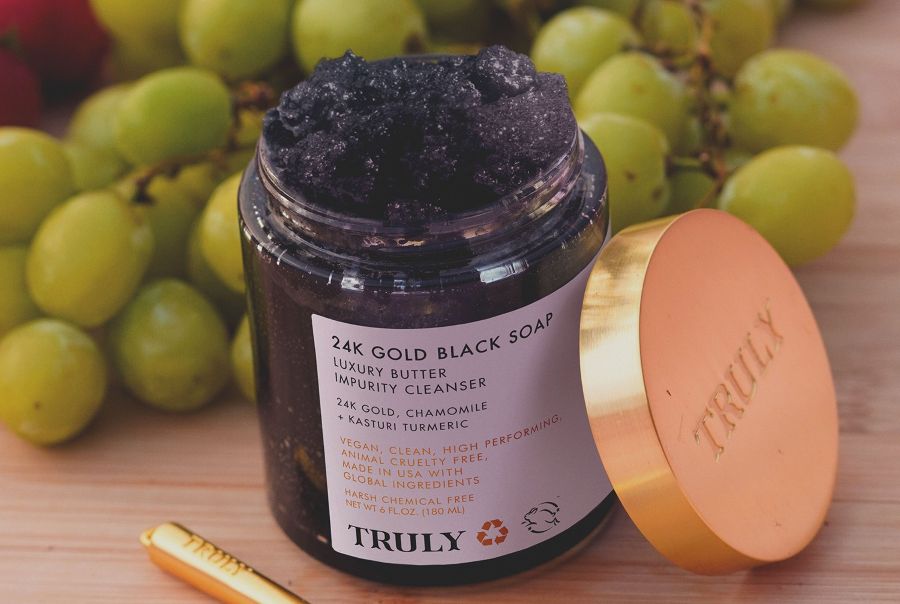 best salicylic acid facial cleanser | closeup of open jar of Truly's 24k gold black soap cleanser with bunch of grapes in background