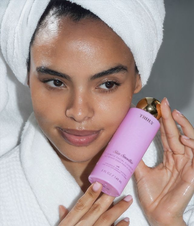 Young woman in white bathrobe holding Truly's Smoothie Cleanser as part of her winter skincare routine