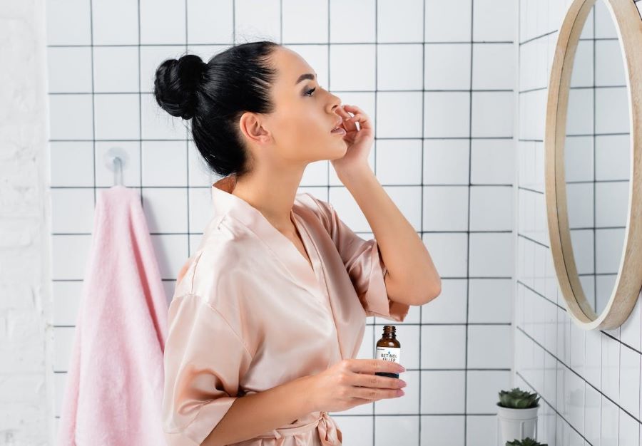 Can You Use BHA with Retinol? | Woman in bathroom applying serum in front of mirror