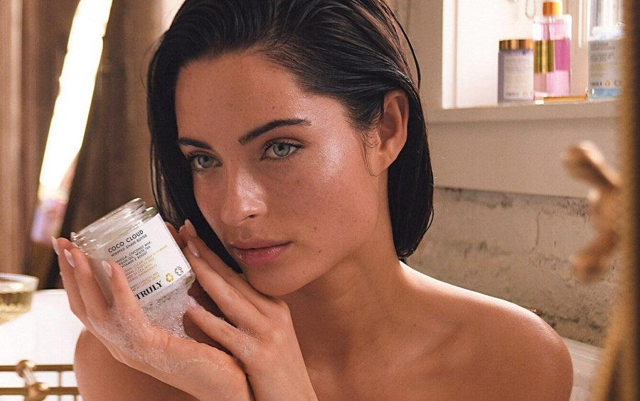 coconut milk benefits for skin | Dark haired woman in bath holding jar of Truly's coco cloud shave butter