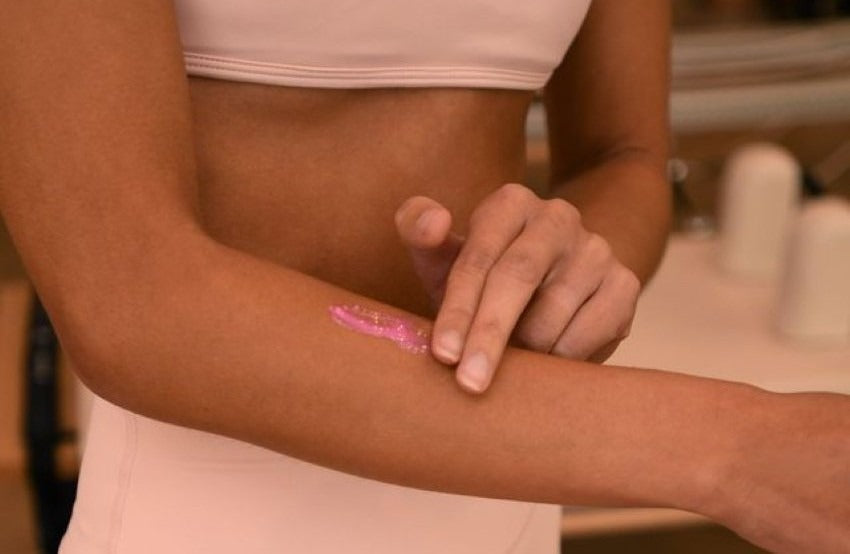 how to get rid of arm pimples | A close-up shot shows a person wearing a light pink top applying a streak of pink serum to their inner forearm.