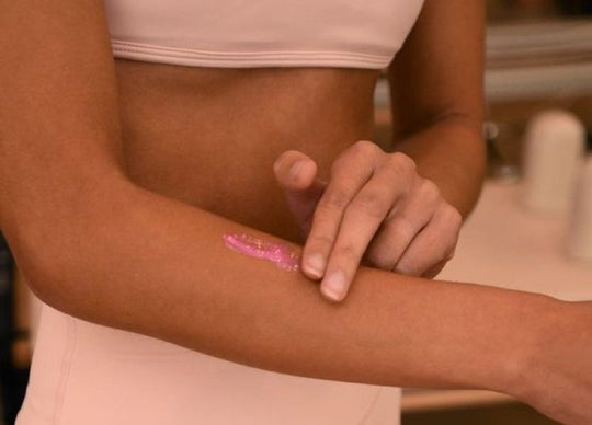leg acne | Woman in pink sports bra holds bottle of Truly's Smooth Legend Serum with 4 pink droplets on leg