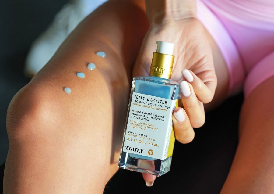Woman's hand holding Truly's jelly booster pigment body potion for dark spots on bikini line with four drops on thigh 