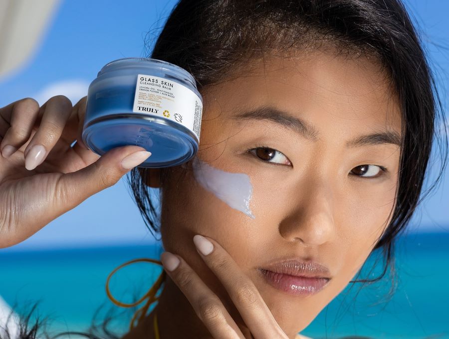 how to get rid of oily skin | young dark haired woman holding truly's glass skin facial cleanser with swatch on face