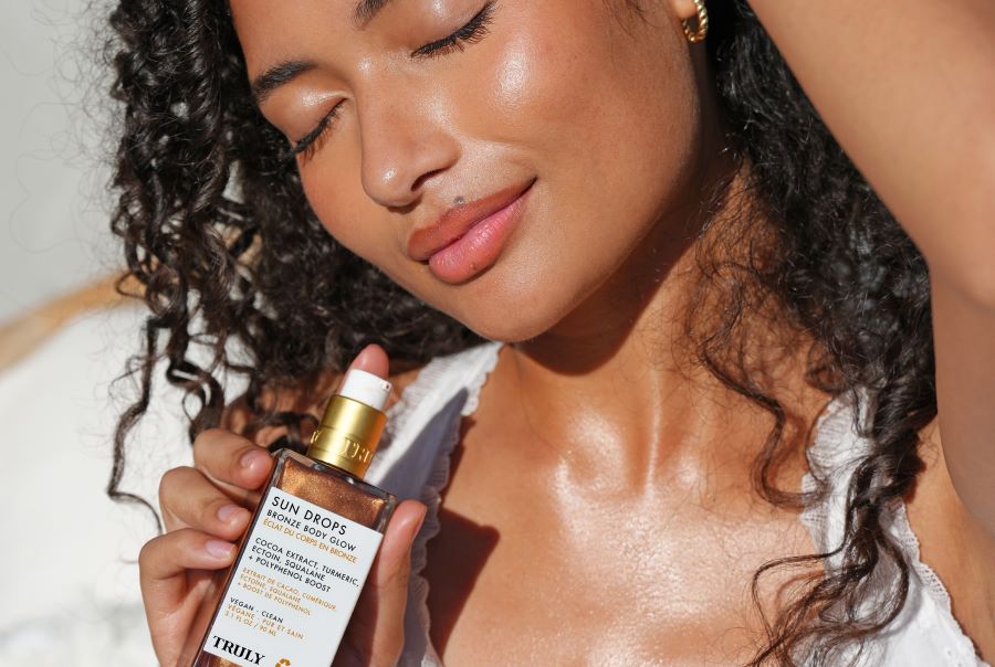 how to get rid of tan lines | young woman with dark curly hair holding truly beauty's sun drops bronzing oil