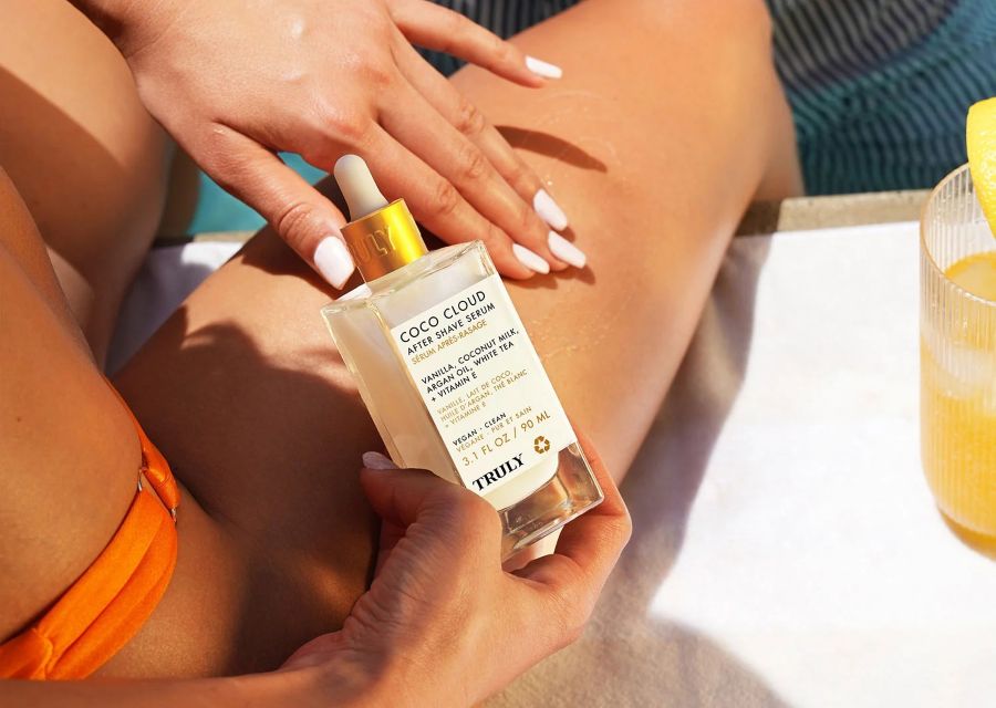 how to shave bikini line | woman in orange bikini applying truly coco cloud after shave serum to leg