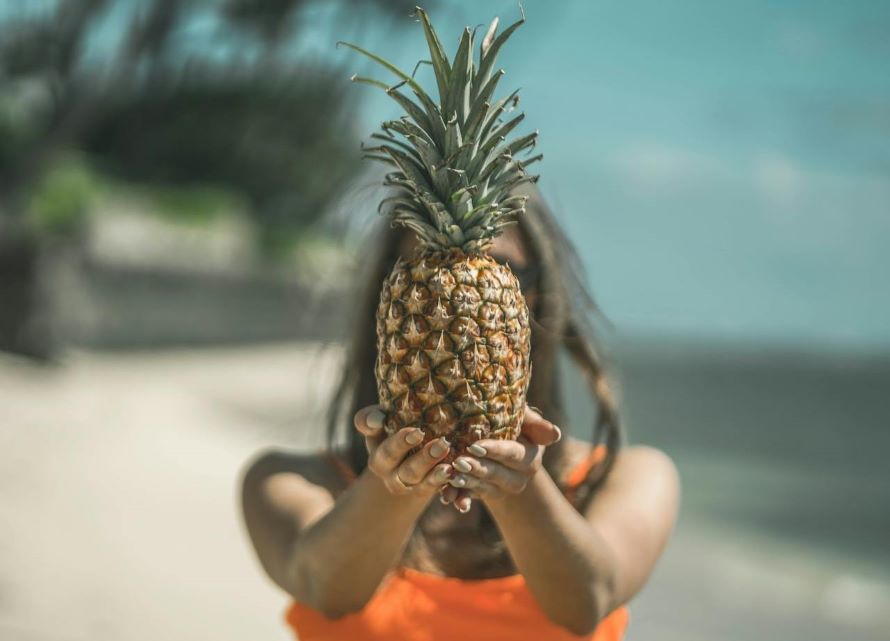 is pineapple good for your skin? | woman on beach holding pineapple in front of face