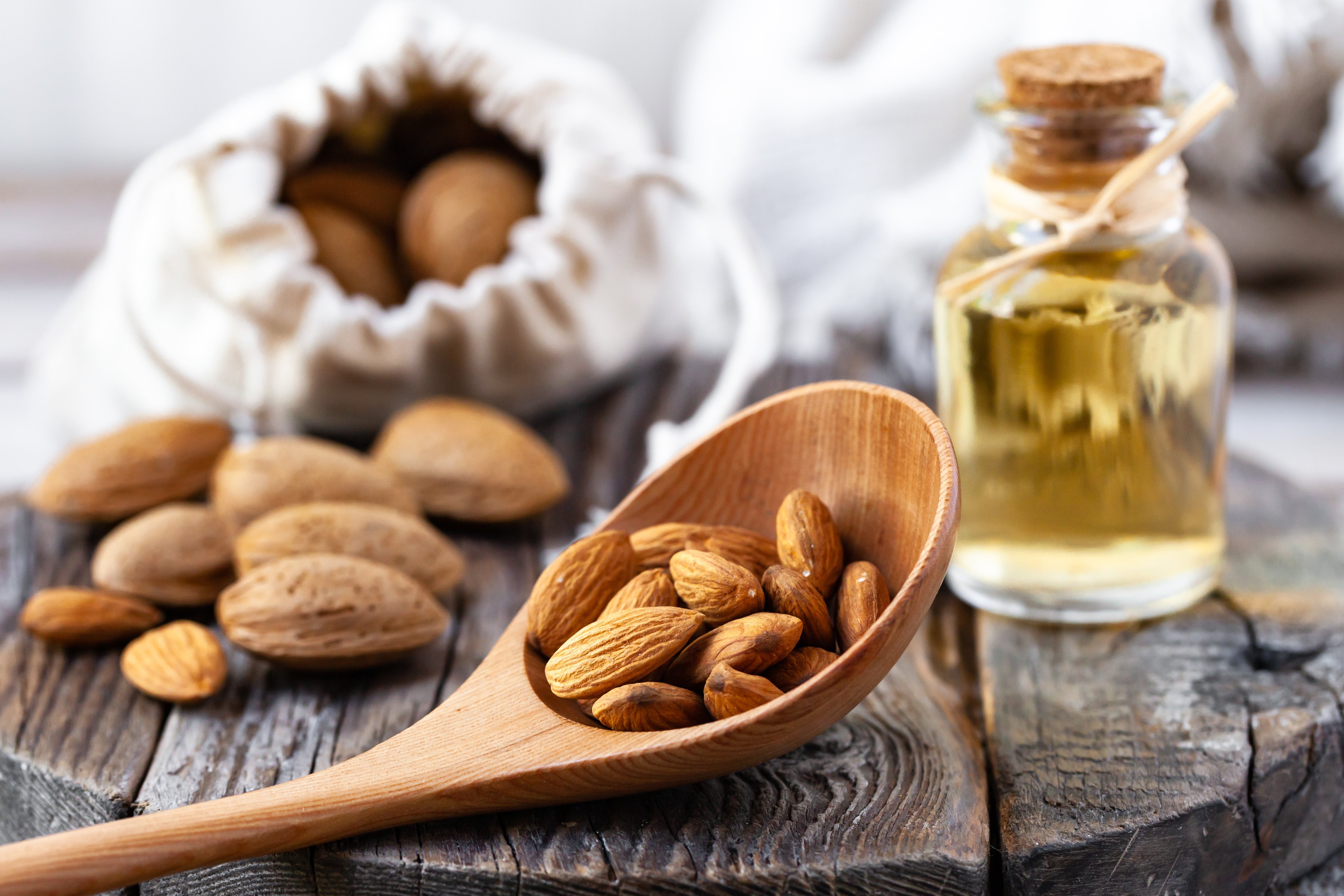 wooden table featuring wooden spoon with almonds and bottle of almond oil