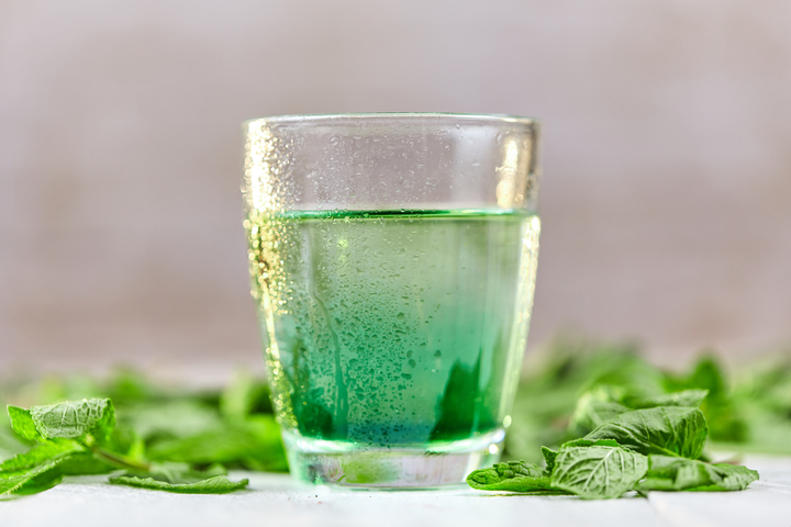 a glass of water infused with liquid chlorophyll, surrounded by fresh mint leaves