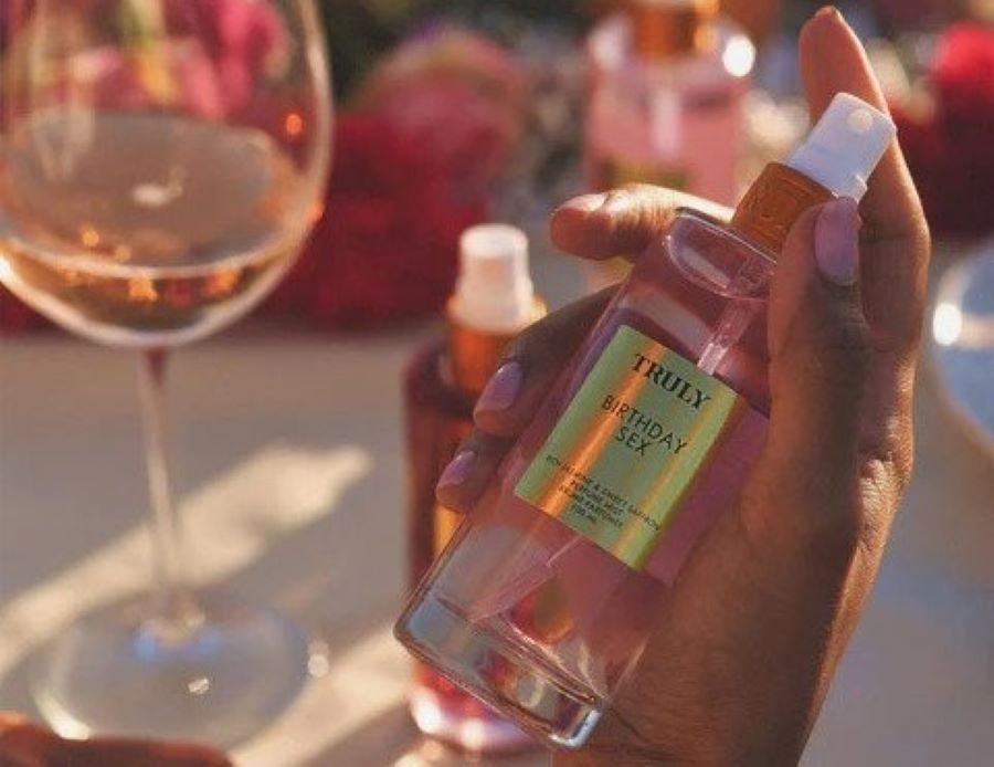 how to layer fragrances | Truly's birthday sex perfume mist held in front of table with wine glass