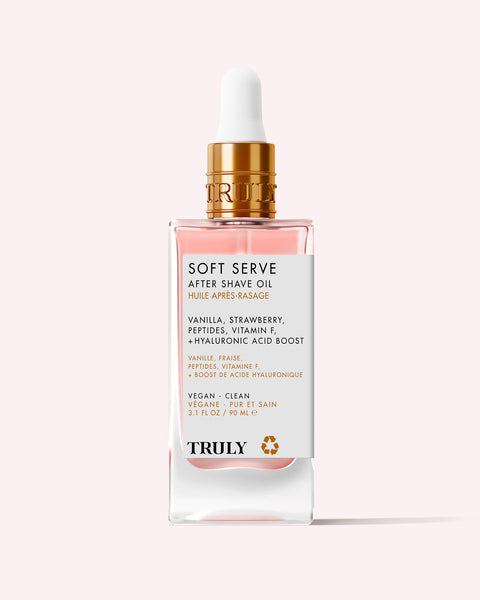 A glass dropper bottle labeled Soft Serve After Shave Oil by Truly Beauty with gold accents sits on a light pink background, featuring vanilla, strawberry, peptides, vitamin F, and hyaluronic acid for soothing after shave care and ingrown hair treatment.