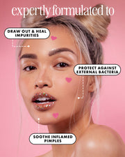 A blonde woman with a bun poses against a pink backdrop, wearing heart stickers from Truly Beauty's #Heart Your Imperfections Blemish Patches, which use hydrocolloid to treat blemishes by drawing out impurities and soothing inflamed pimples.
