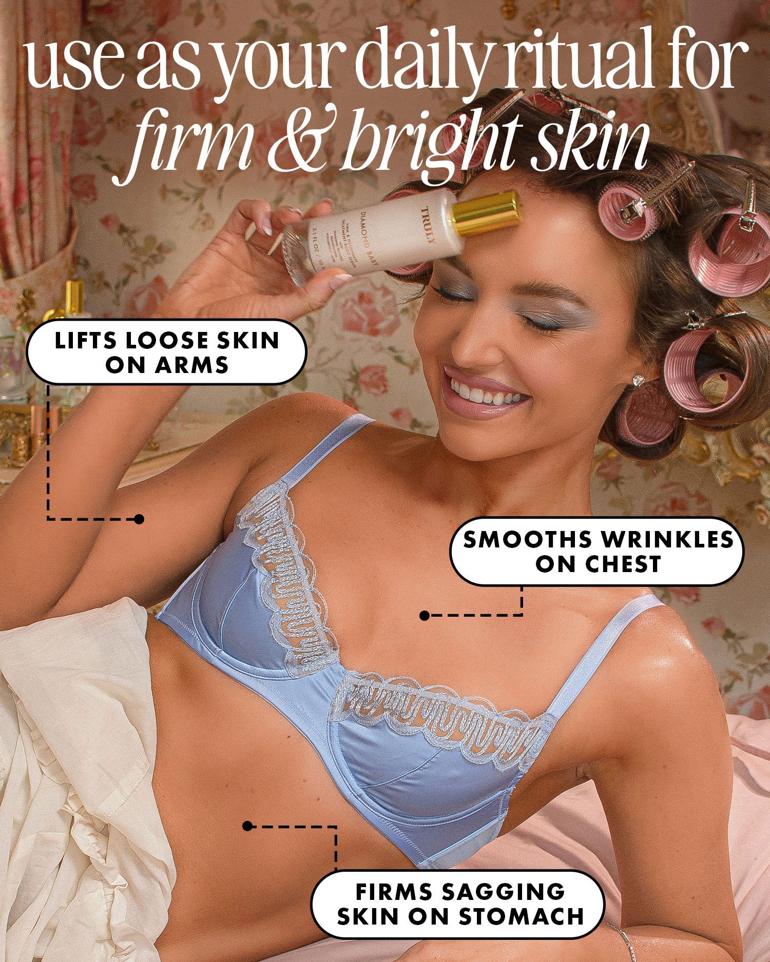 A smiling woman in a blue bra and pink rollers applies Diamond Baby Treatment Body Serum by Truly Beauty to her forehead. Text highlights its benefits: lifting loose arm skin, smoothing chest wrinkles, and firming sagging stomach skin.