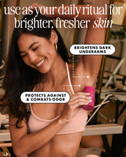 A smiling woman applies Truly Beauty’s Unicorn Fruit Skin Brightening and Smoothing Deodorant to her underarm, highlighting brighter skin and odor protection with this aluminum-free, niacinamide-infused formula in a vibrant, modern room.