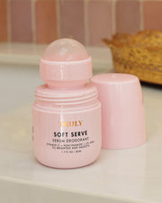 A pink Truly Beauty Soft Serve Serum Deodorant sits open on a bathroom counter, its cap nearby. Infused with vitamin C, niacinamide, and AHA, this deodorant helps brighten and smooth your underarms.