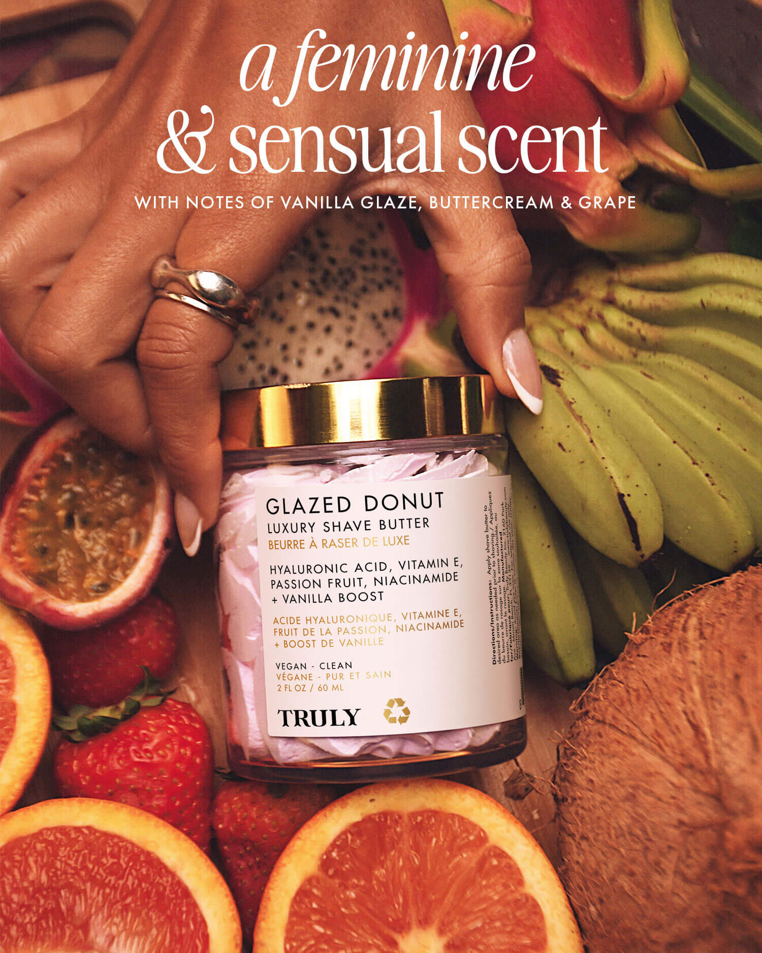 A jar of Truly Beautys Glazed Donut Luxury Shave Butter sits among tropical fruits and leaves. Text highlights its feminine, sensual scent—vanilla glaze, buttercream, grape—and a hydrating formula with hyaluronic acid.