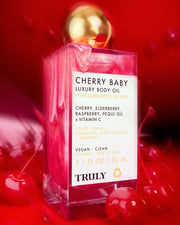 A bottle of Truly Beauty’s Cherry Baby Luxury Body Oil with a gold cap rests among fresh cherries. This pink, shimmery oil hydrates and adds glow with cherry, elderberry, raspberry, pequi oil, and vitamin C.