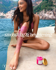 A woman in a pink bikini sits on a dock by the water, smiling as she applies Truly Beauty’s Smooth Legend Pre-Shave Scrub to her leg. Text reads “smoothing & brightening” with product and ingredients shown beside her for glowing skin.