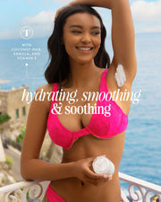 A smiling woman in a bright pink bikini applies Coco Cloud Luxury Shave Butter by Truly Beauty to her underarm on a seaside balcony. Text highlights hydrating, smoothing effects with coconut milk and shave butter to help prevent ingrown hairs.