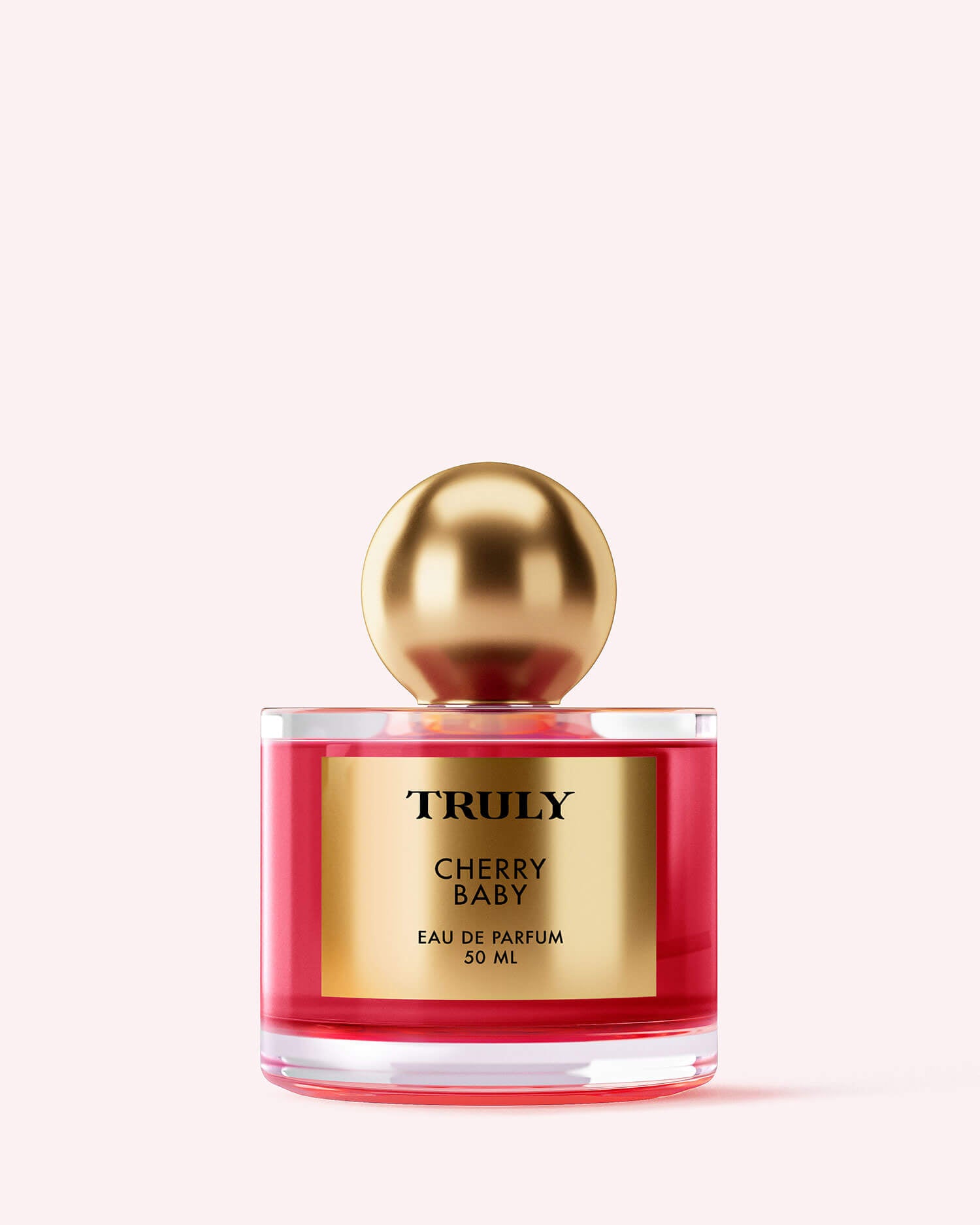 A 50ml bottle of Truly Beauty Cherry Baby Eau De Parfum, with pink-red fragrance featuring black cherry and jasmine, gold label, and large gold spherical cap, displayed on a light pink background.