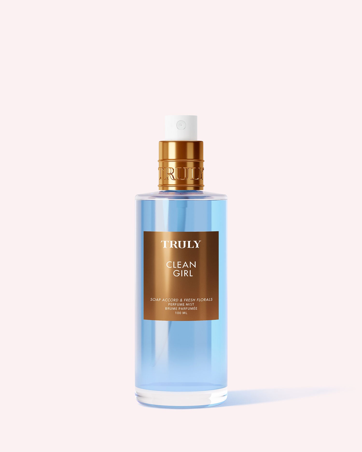 A clear spray bottle with blue liquid labeled Clean Girl Perfume Mist by Truly Beauty, topped with a gold cap, stands on a light pink background; this fragrance blends fresh florals with white musk.