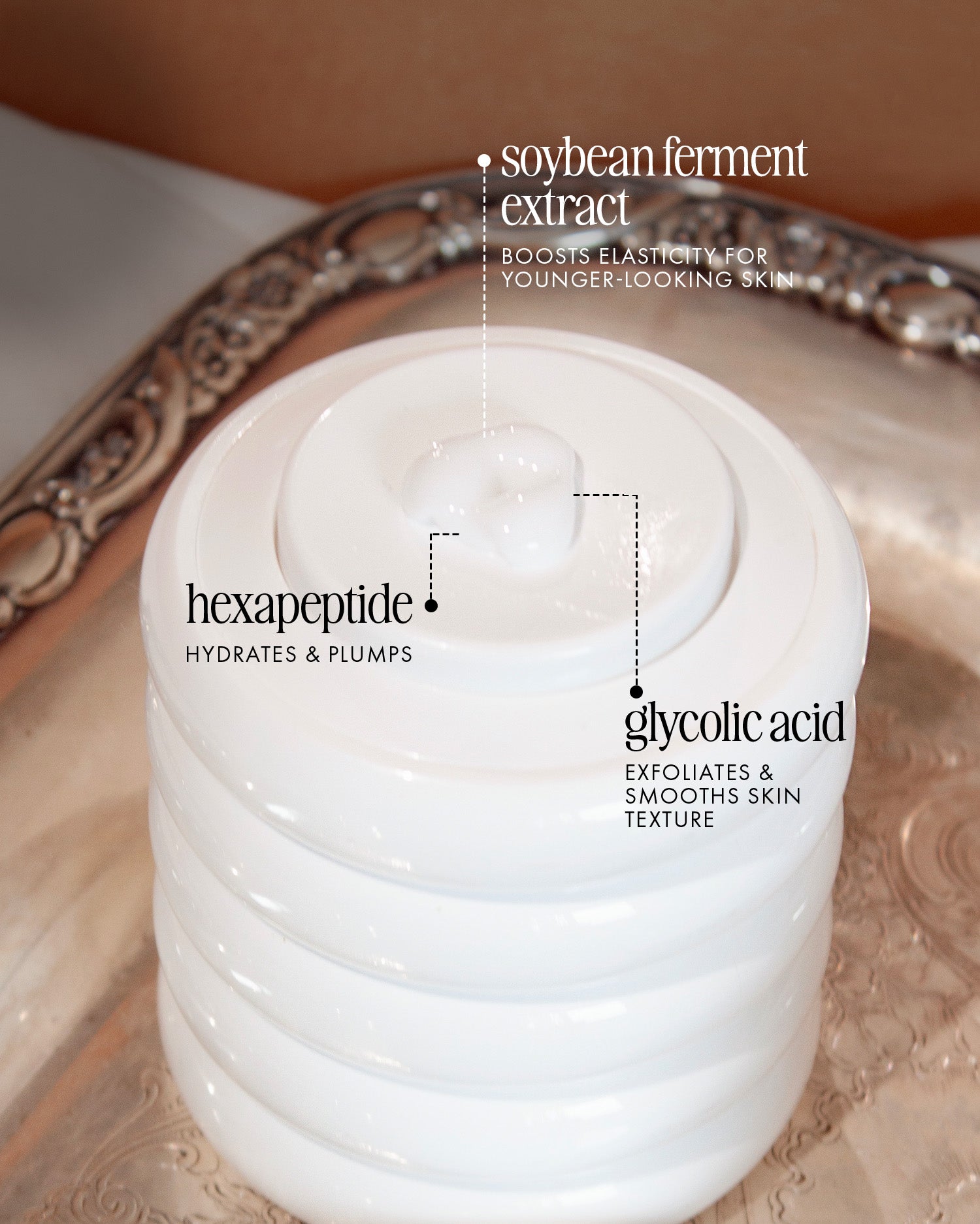 A white lidded jar of Truly Beauty’s Cloud Cream Pro-Peptide Facial Moisturizer sits on a silver tray. Overlaid text highlights key ingredients: soybean ferment extract, hexapeptide, and glycolic acid.