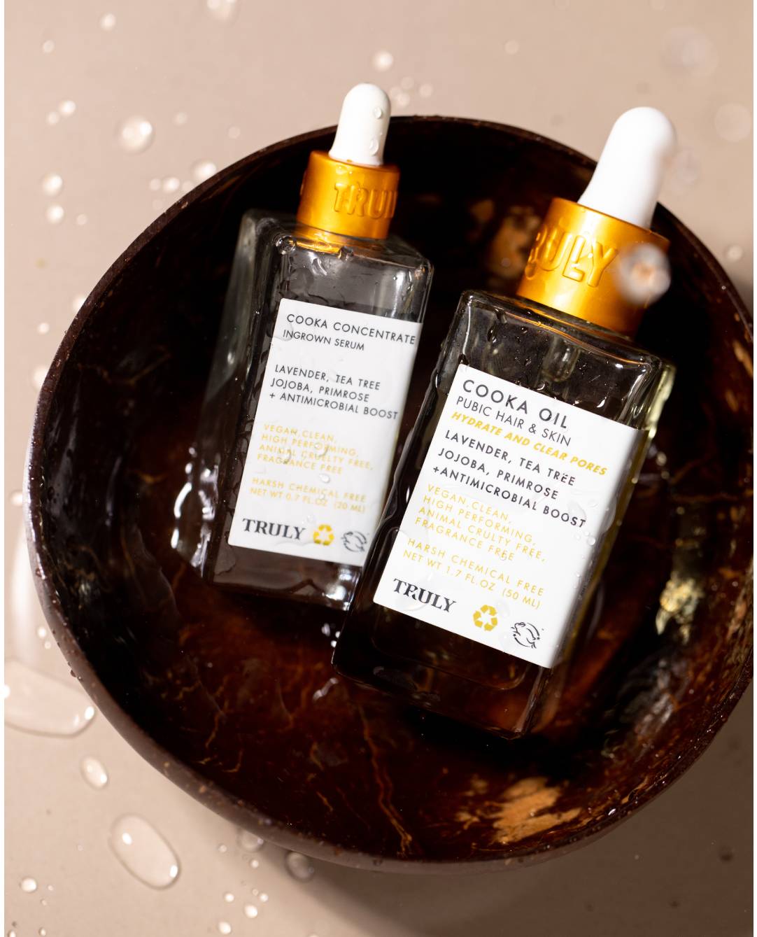 Two glass dropper bottles labeled Truly Beauty with gold caps sit in a brown coconut shell bowl. The front labels read Ultimate Cooka Treatment, surrounded by water droplets. Perfect companions for your next self-care ritual.