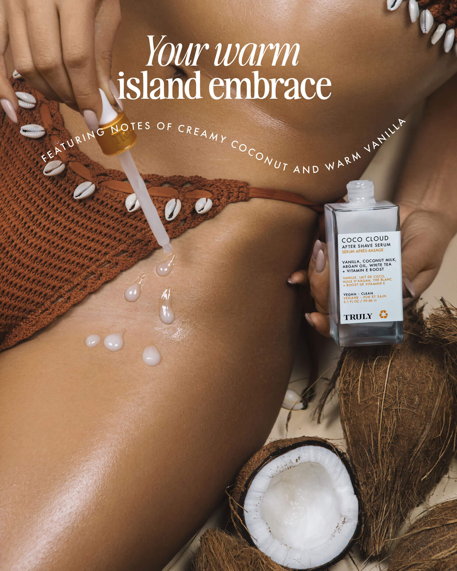 A hand drops hydrating argan oil onto a woman’s tan skin as she lounges in a brown crochet swimsuit with shells, holding Truly Beauty’s Coco Cloud After Shave Serum beside an open coconut. Text: Your warm island embrace.