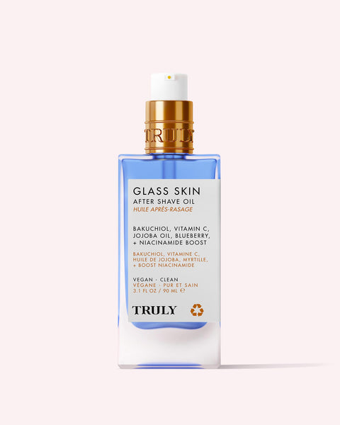A clear bottle of Truly Beauty’s Glass Skin After Shave Oil with a blue base and gold pump. The label features bakuchiol, vitamin C, jojoba oil, blueberry, and niacinamide for a vegan, clean formula that delivers glass skin.