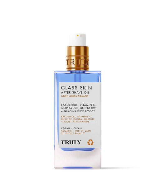 A clear bottle of Truly Beauty’s Glass Skin After Shave Oil with a blue base and gold pump. The label features bakuchiol, vitamin C, jojoba oil, blueberry, and niacinamide for a vegan, clean formula that delivers glass skin.